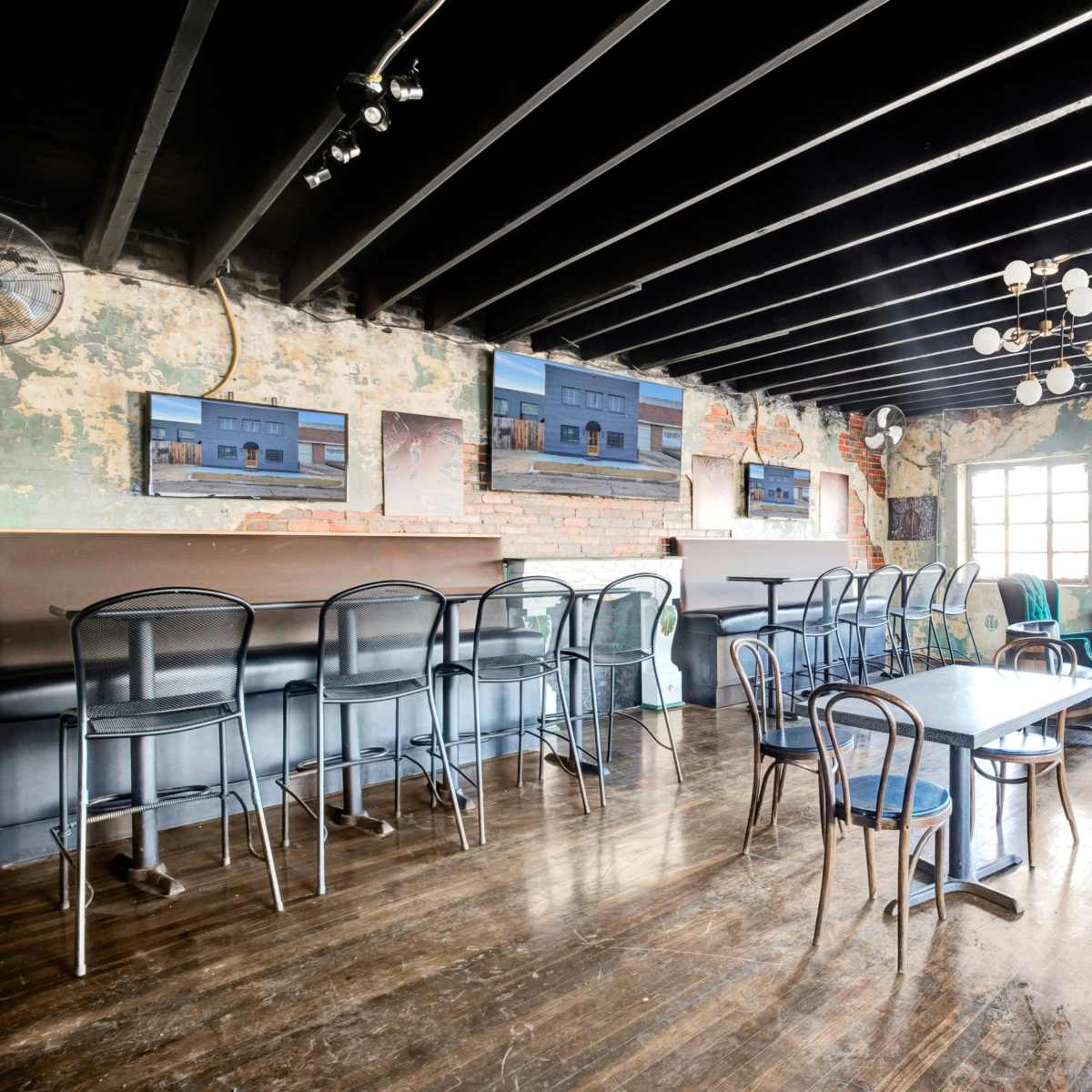 A spacious, rustic room with a bar area, several tables, and a mix of seating arrangements, including chairs and a green couch, with exposed brick and peeling walls.