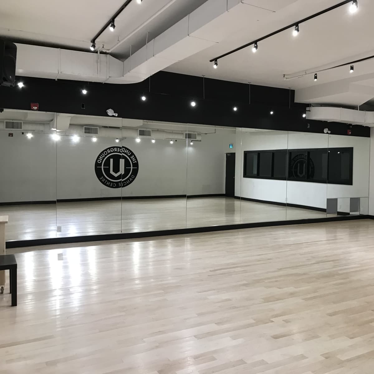 A spacious dance studio with a wooden floor, large mirrors on one wall, and black and white decor.