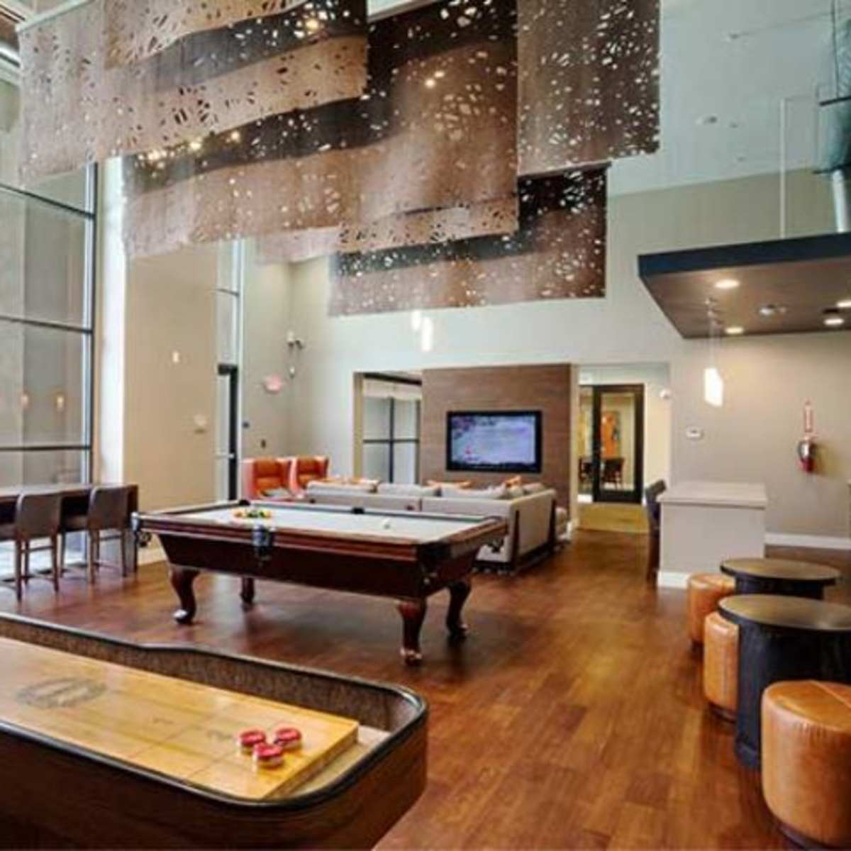 A spacious indoor recreation area featuring a pool table, shuffleboard, and a large television, with modern furniture and large windows.