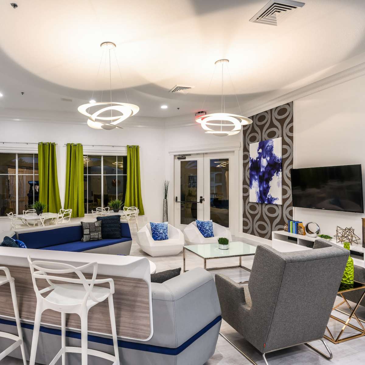A modern living space featuring a sectional sofa, decorative chairs, a television, and large windows dressed with bright curtains.