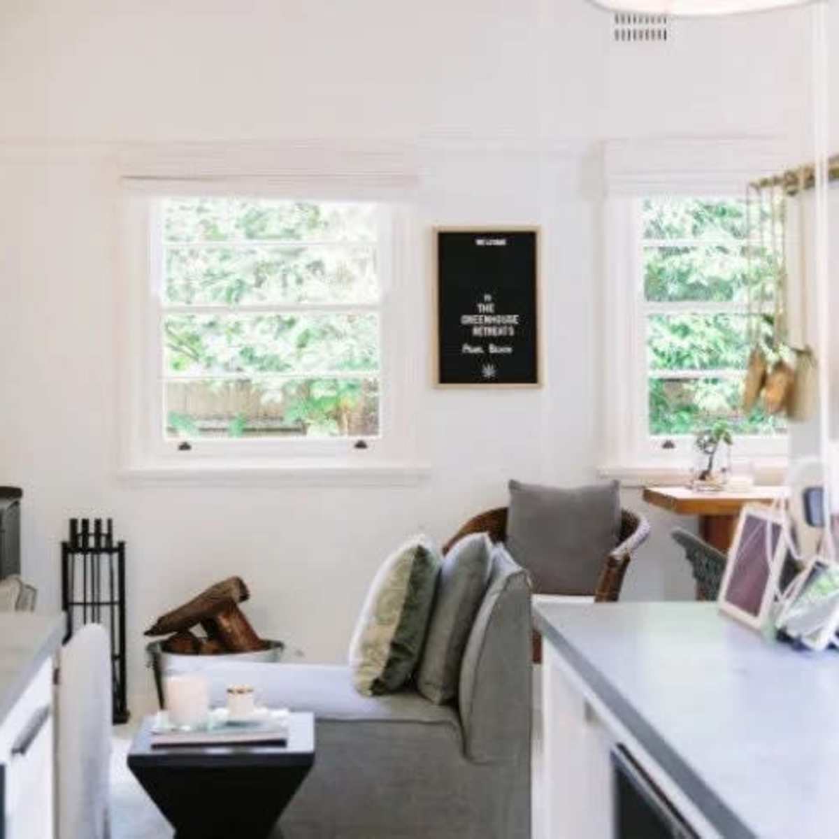 A cozy living space featuring a gray sofa, a small black side table, and a wood stove in front of a window with greenery outside.