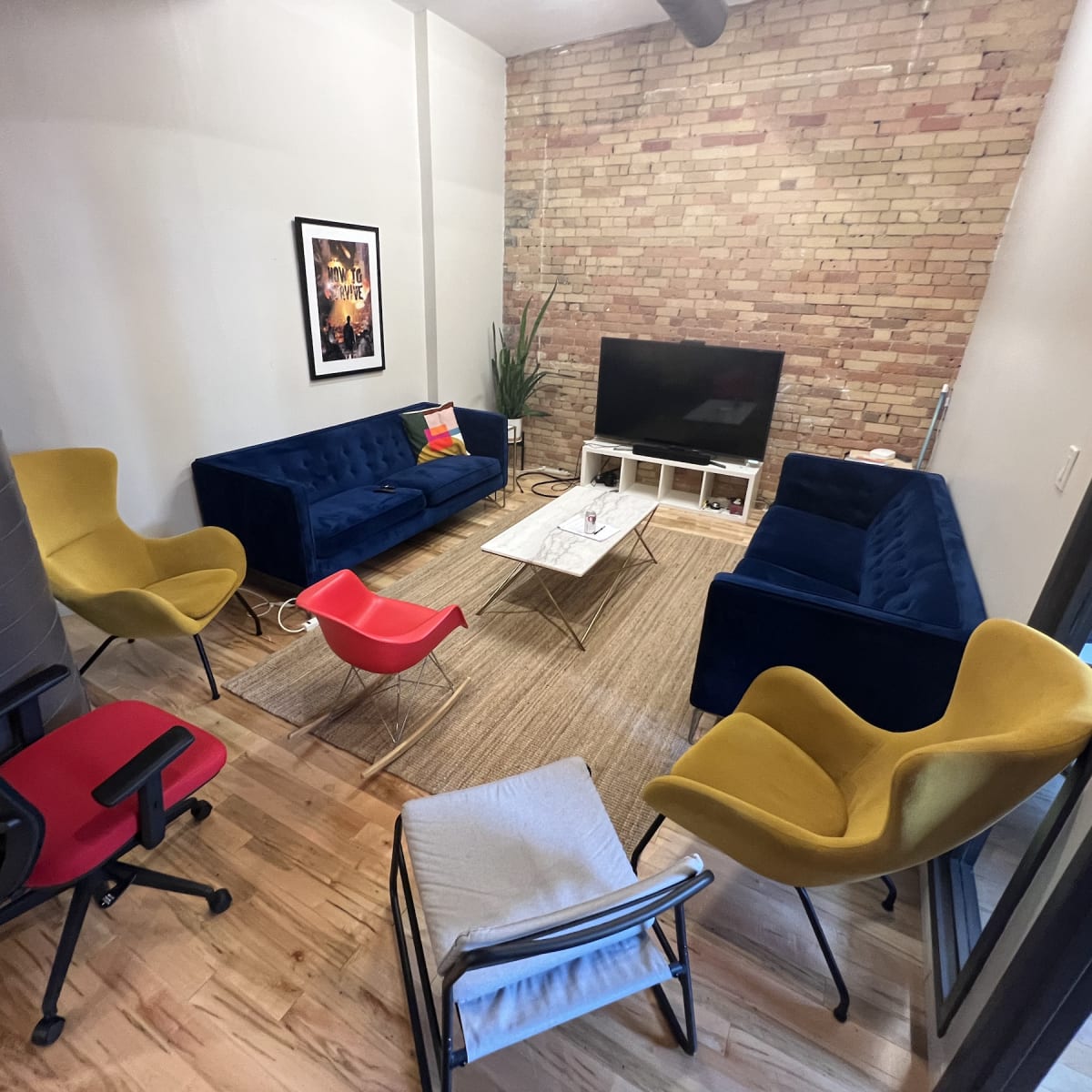 A modern lounge area features blue and yellow seating, a television on a white stand, and a textured brick wall.