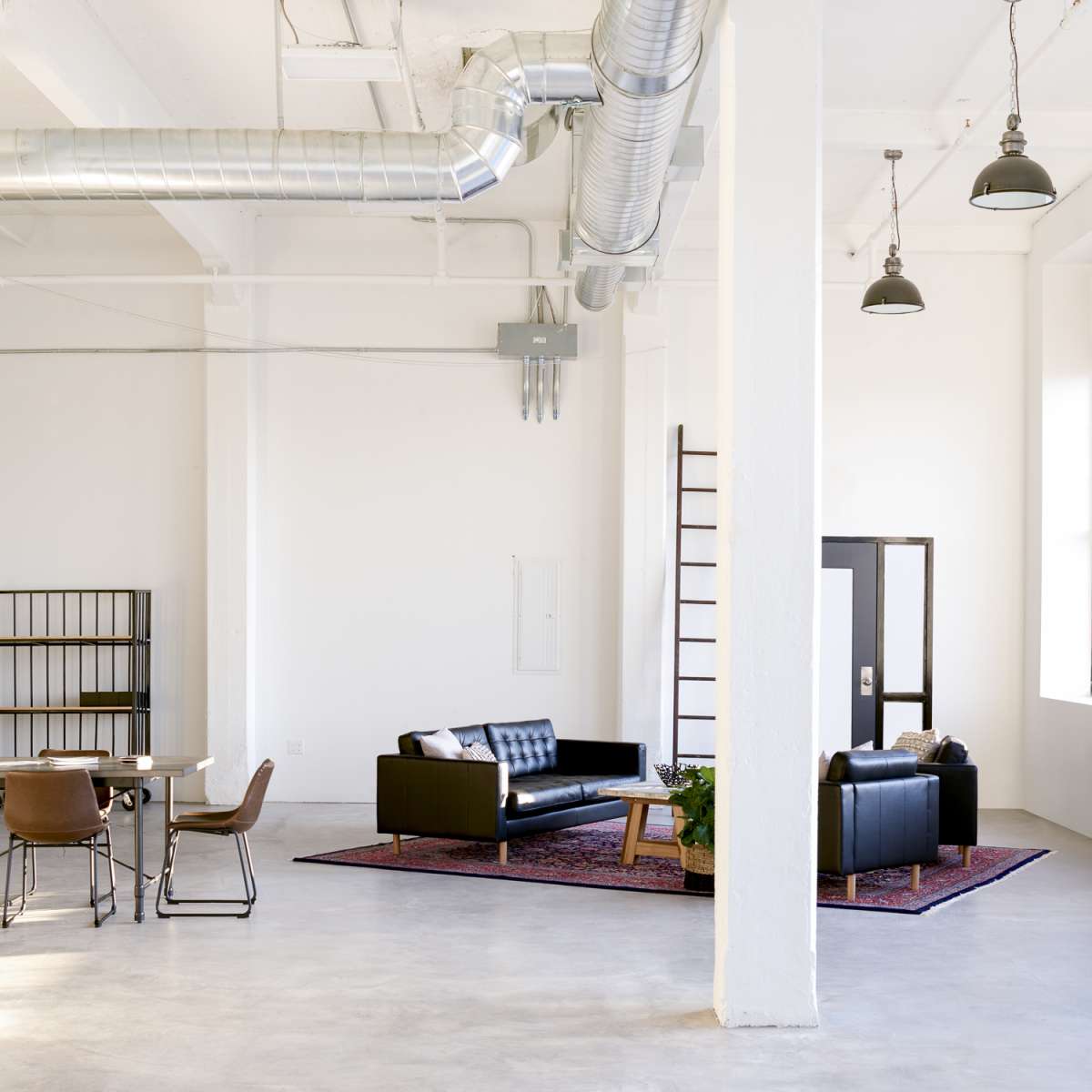 A spacious, modern room with a black sofa, a dining table, and industrial-style elements.