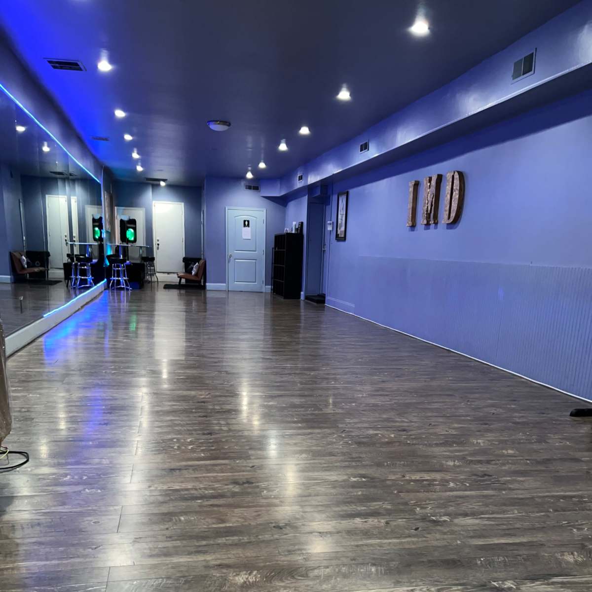 An empty dance studio with wooden flooring, mirrors along one wall, and ambient lighting.