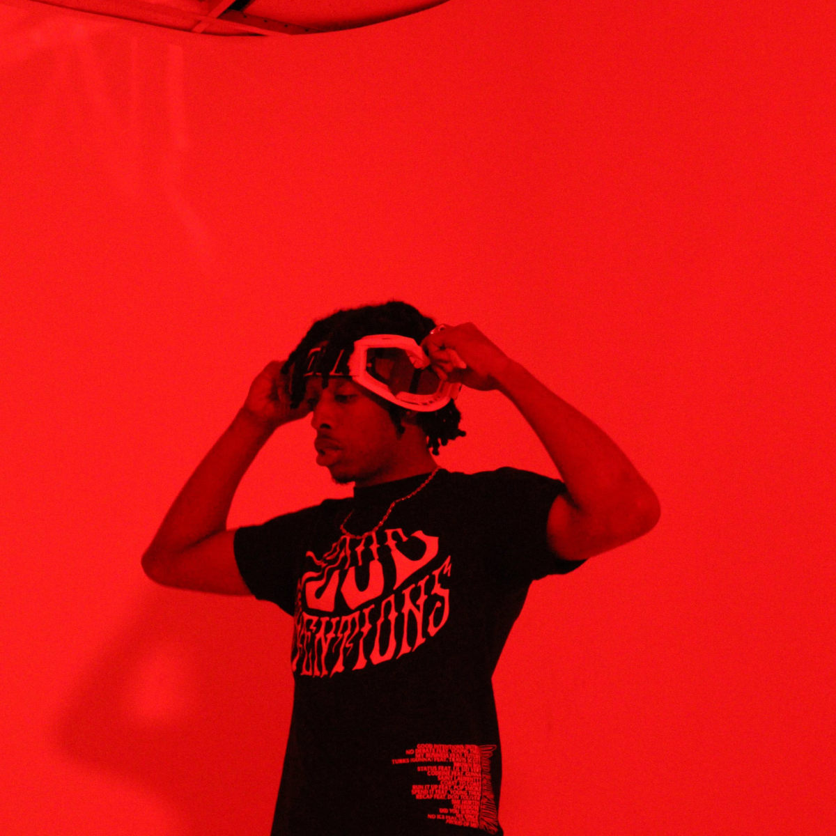 A person wearing a black t-shirt and headphones stands in front of a red backdrop.