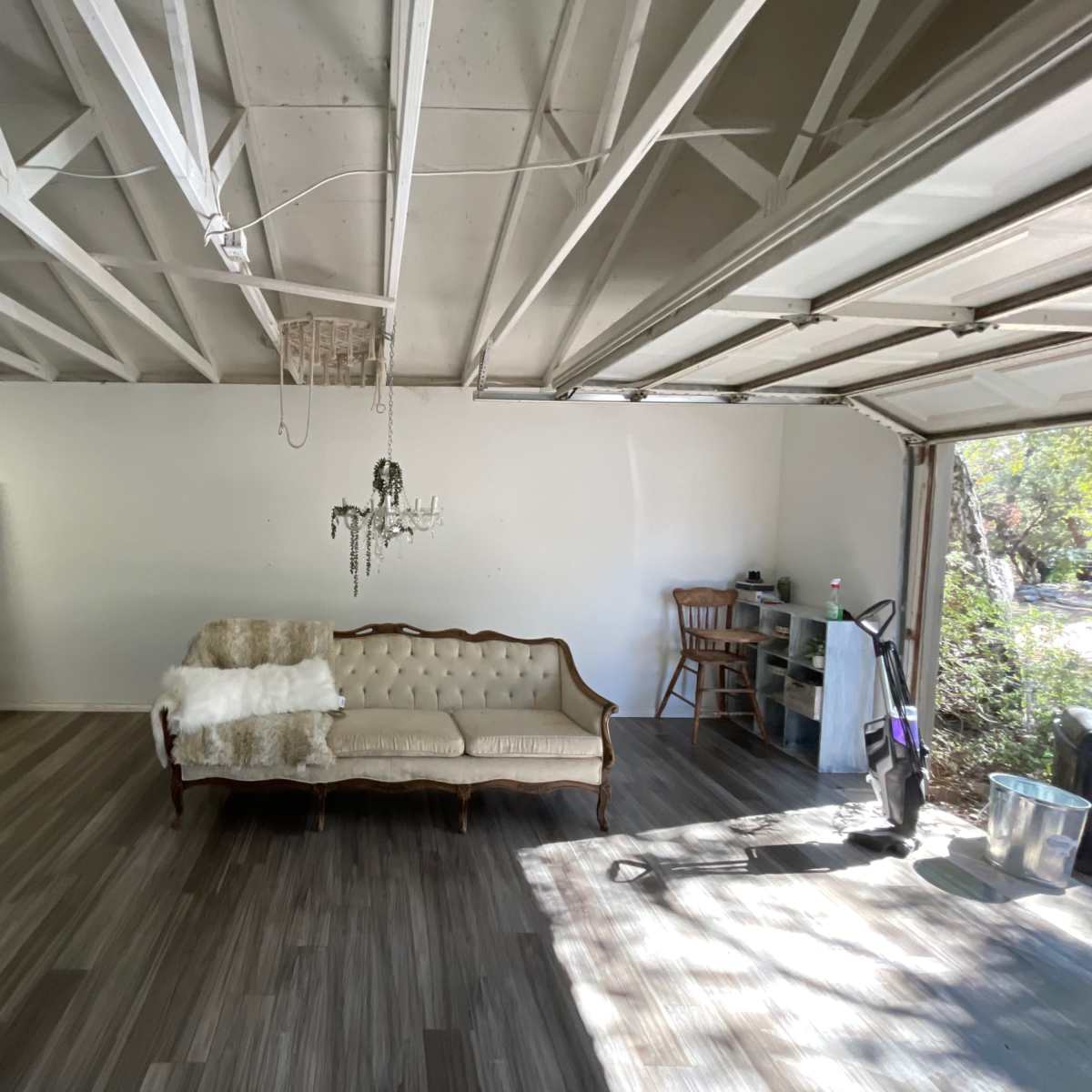 A bare garage features a couch, a toilet, a chandelier, and various pieces of furniture against white walls.