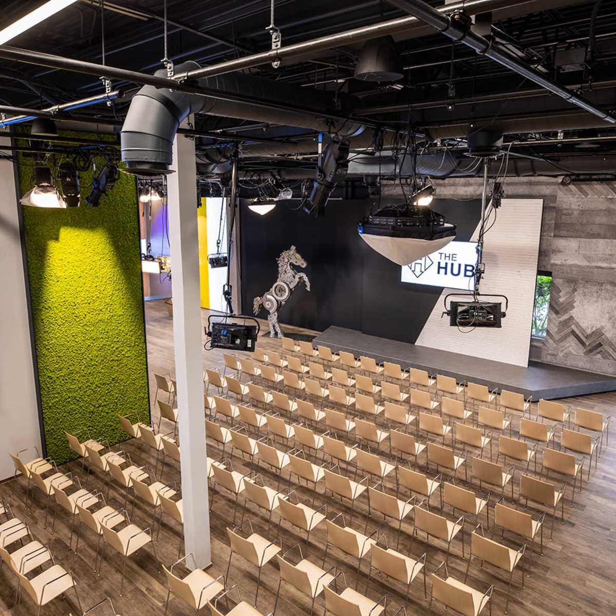 A modern auditorium space with rows of beige chairs set up in front of a stage featuring a large screen and a decorative sculpture.