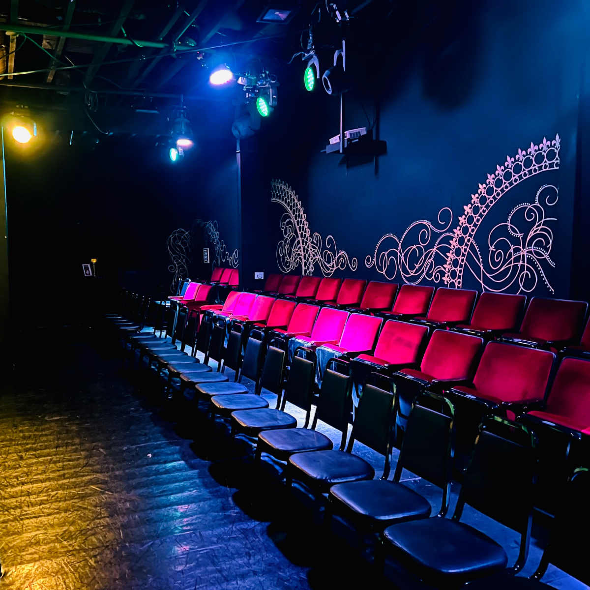 A dimly lit theater features a row of red and black seats against a black wall decorated with intricate designs.