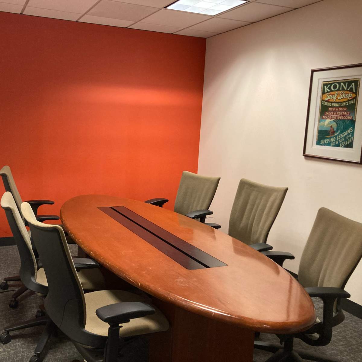A conference room features a wooden oval table surrounded by six chairs and an orange accent wall.