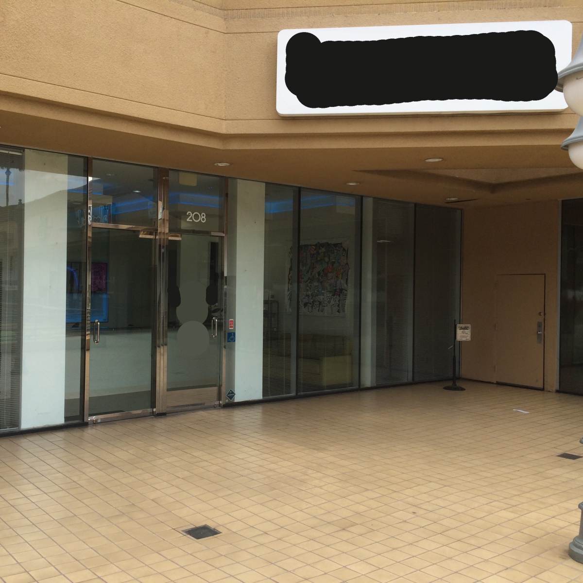 The entrance of a storefront with large glass windows and a tiled walkway in front.