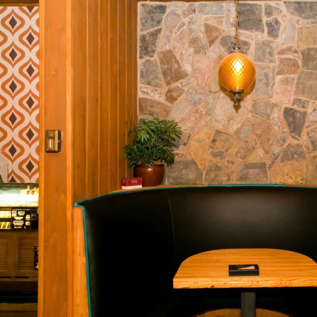 A cozy booth with a wooden table is set against a stone wall and illuminated by a hanging lamp.