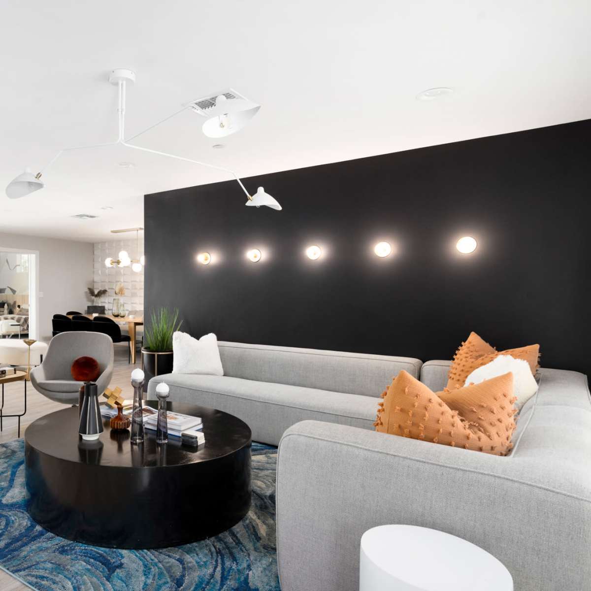 A modern living room with two gray sofas, a round black coffee table, and bright lighting against a dark accent wall.