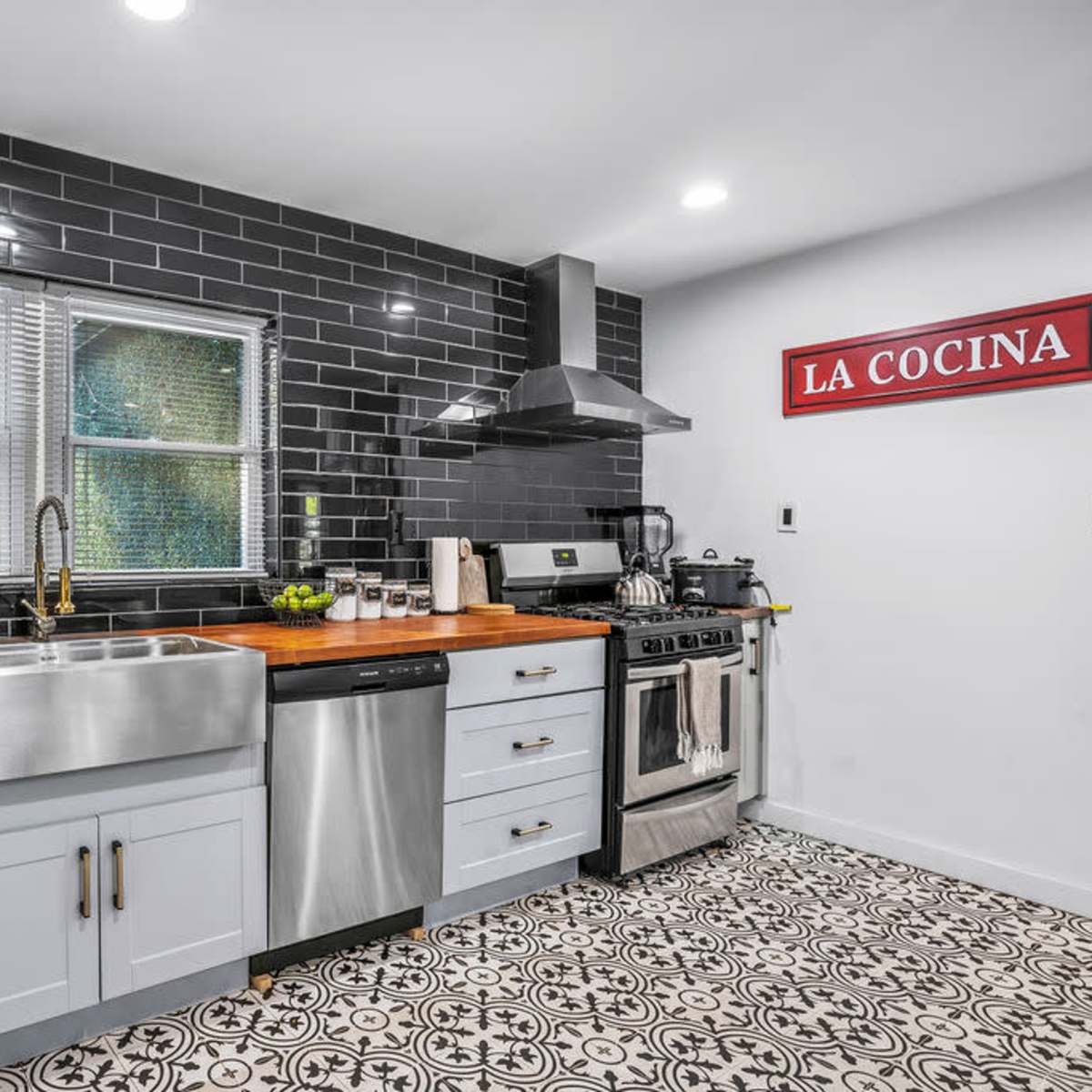 The kitchen features a stainless steel sink, a gas stove, and black subway tile backsplash complemented by patterned flooring.