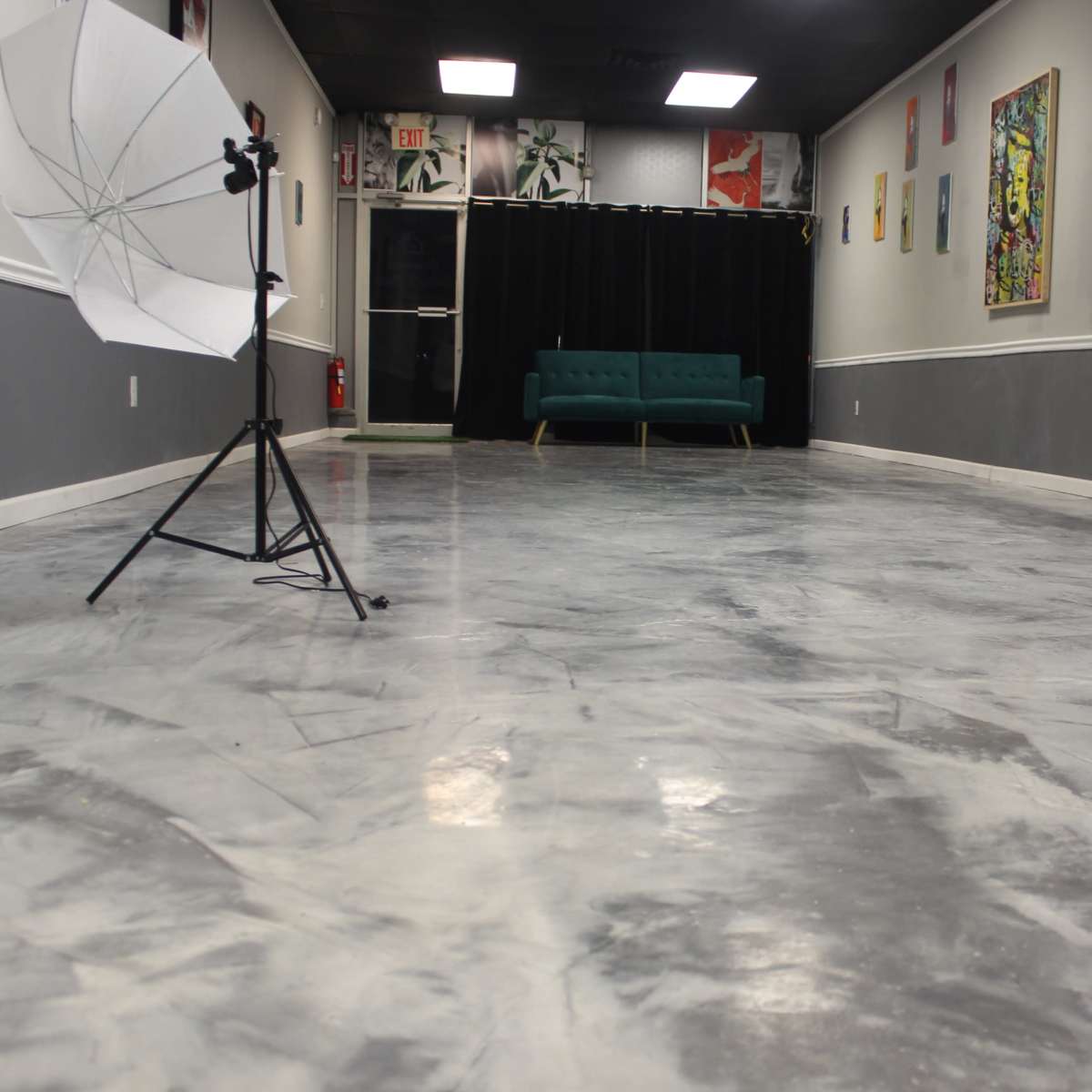 A spacious interior studio with a polished gray floor, a green sofa against a black curtain, and photography equipment placed on either side.