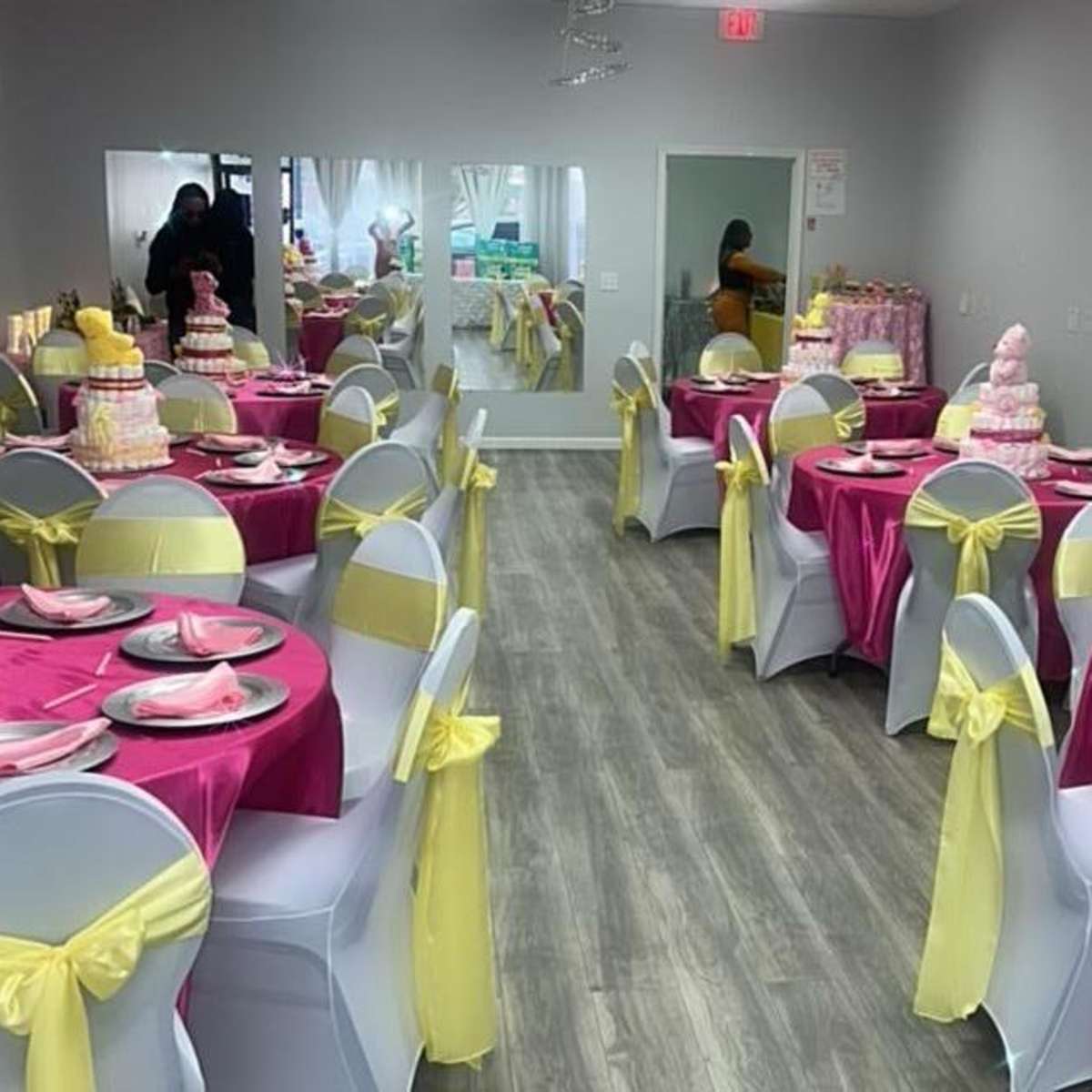 A decorated party room with pink and yellow tablecloths, each set with plates, and featuring multiple multi-tiered cakes on display.