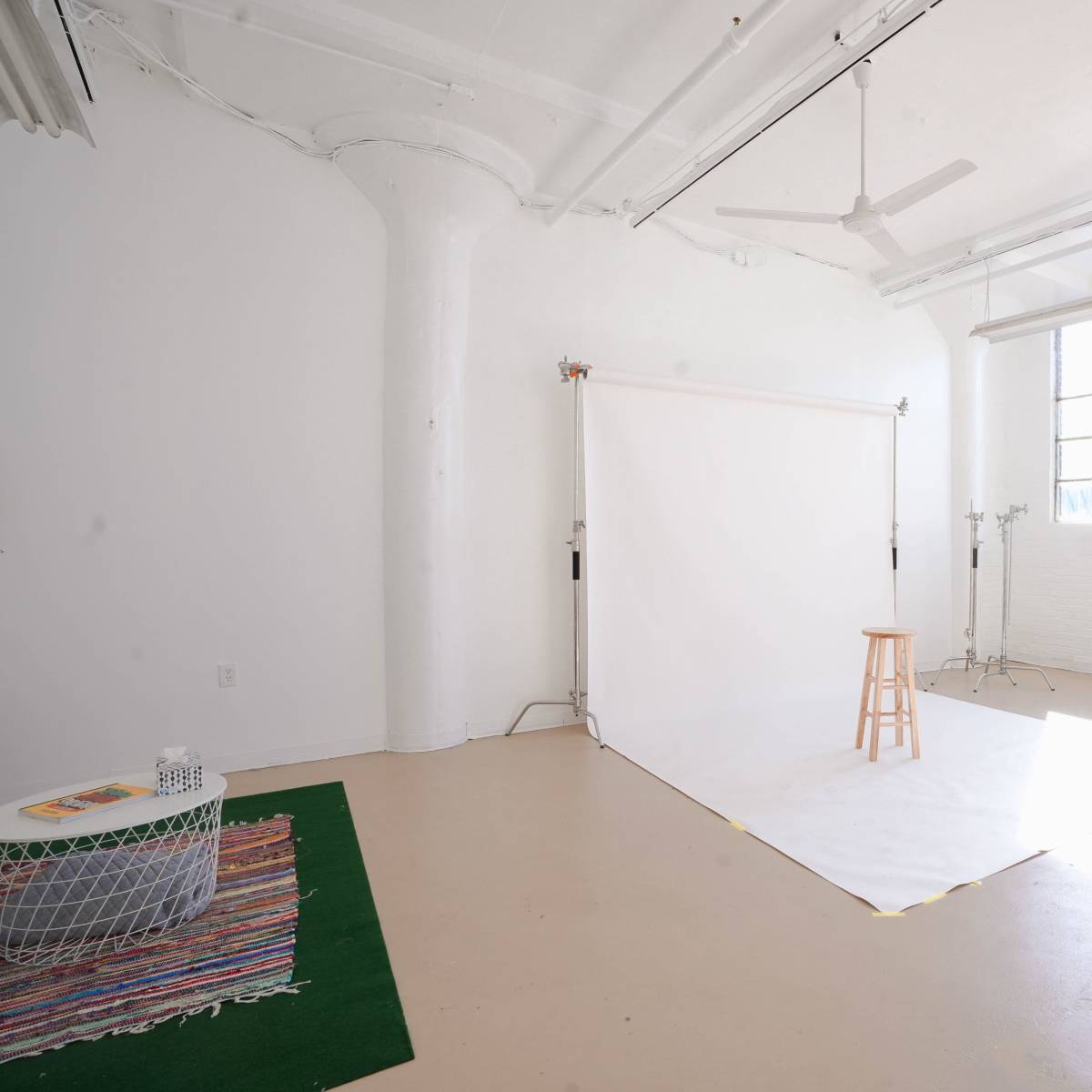 A spacious, well-lit studio with a white backdrop, a wooden stool, and a small table on the floor.