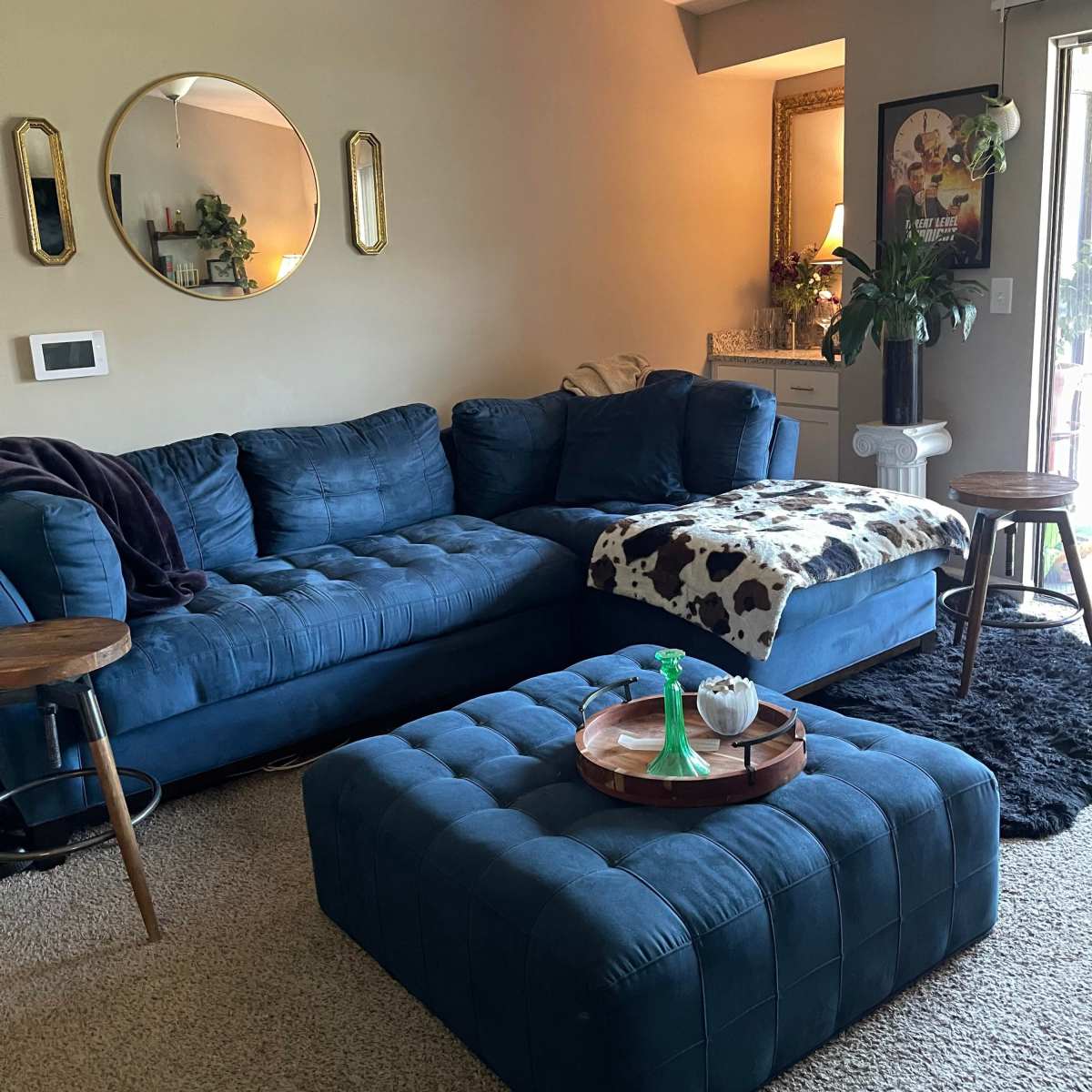 A cozy living room with a blue sectional sofa, a round mirror, a coffee table with decorative items, and a textured rug on the floor.