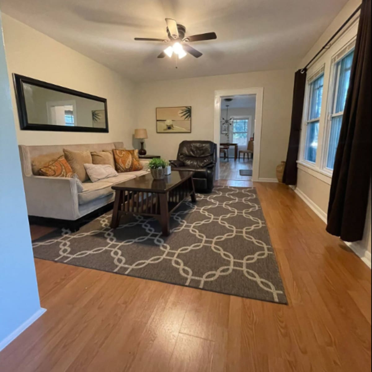 A living room with a sofa and armchair, a coffee table, and a patterned area rug on a wooden floor.