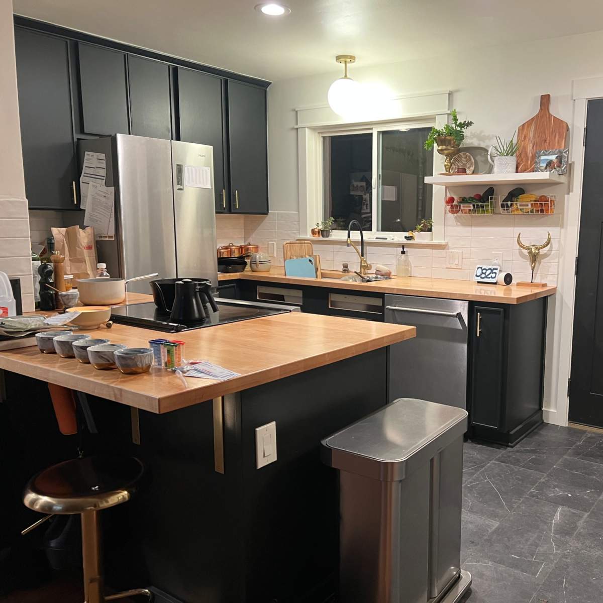 A modern kitchen with black cabinets, a wooden countertop, stainless steel appliances, and an adjacent door leading outside.