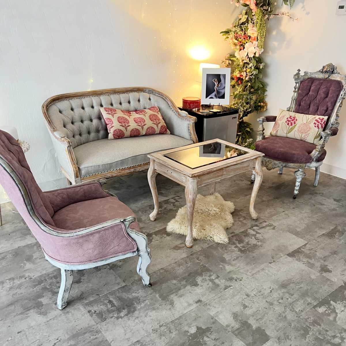 A living room setting with a vintage grey sofa and two purple upholstered chairs arranged around a wooden coffee table on a floor with a grey pattern.