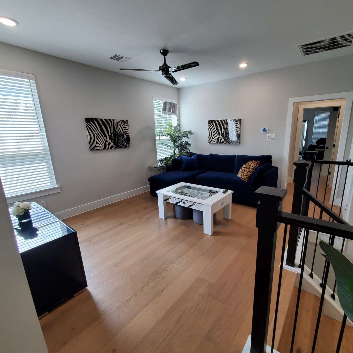 A modern living room featuring a blue sectional sofa, a white coffee table, and decorative wall art, with natural light coming through the windows.