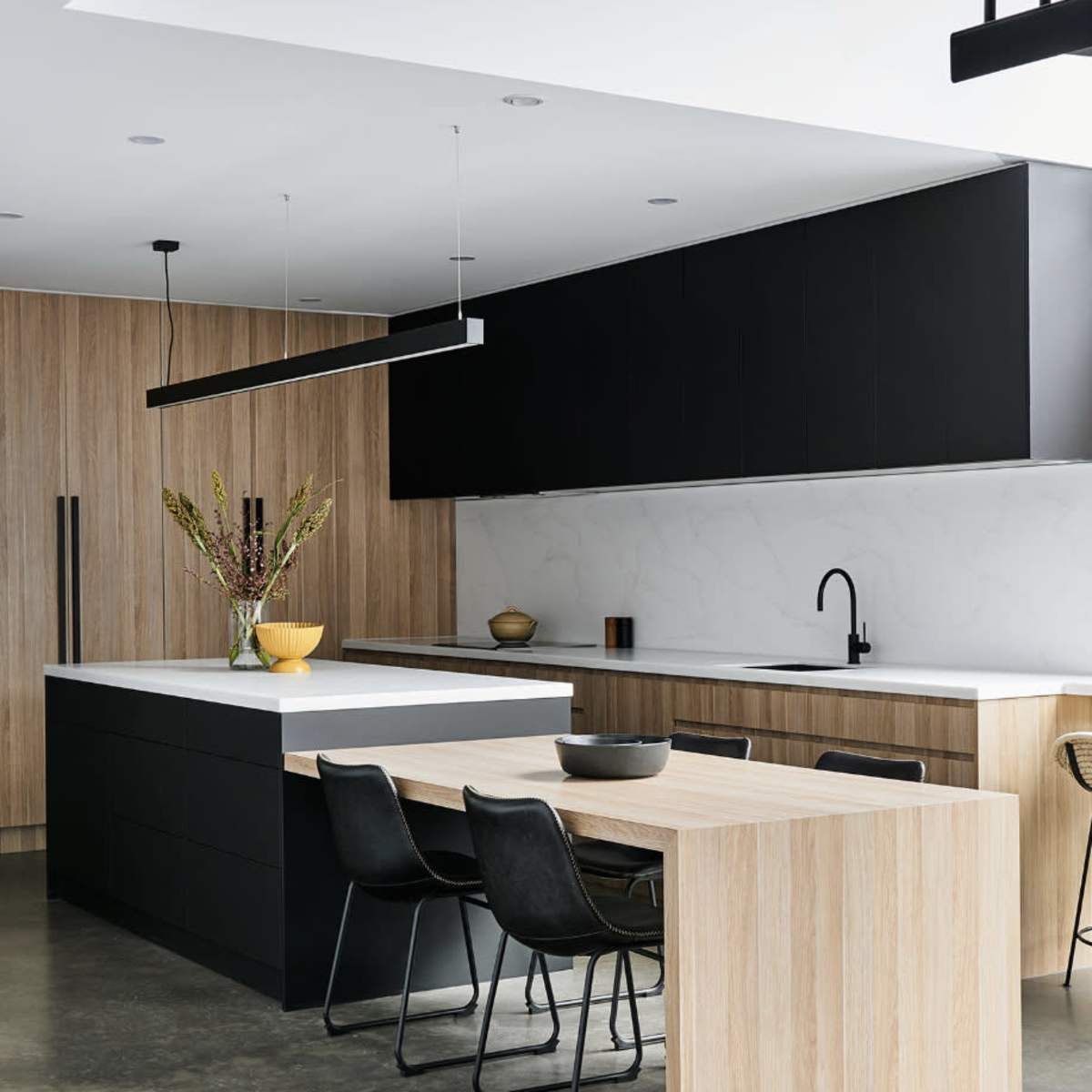 A modern kitchen features a sleek black and wood design with a central island and a dining area.