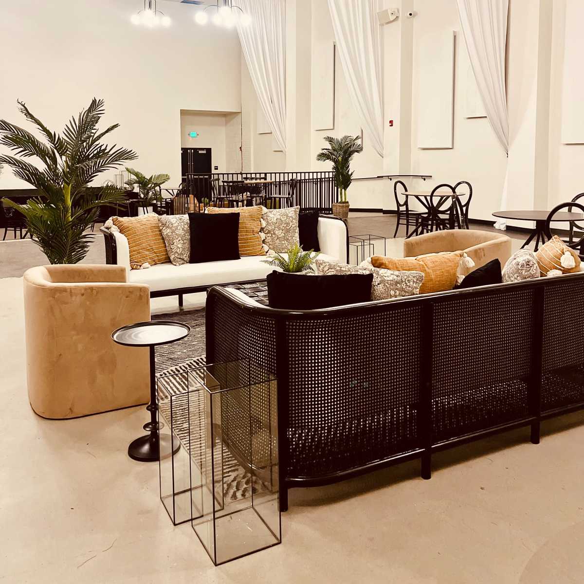A modern, spacious lounge area furnished with sofas, potted plants, and tables, illuminated by overhead lights.