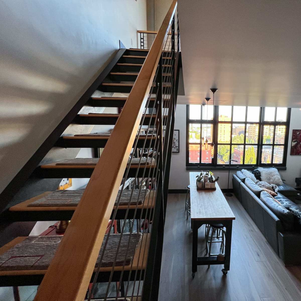 A modern loft space featuring a staircase leading to a loft area, with a living room containing a leather sofa and large windows.