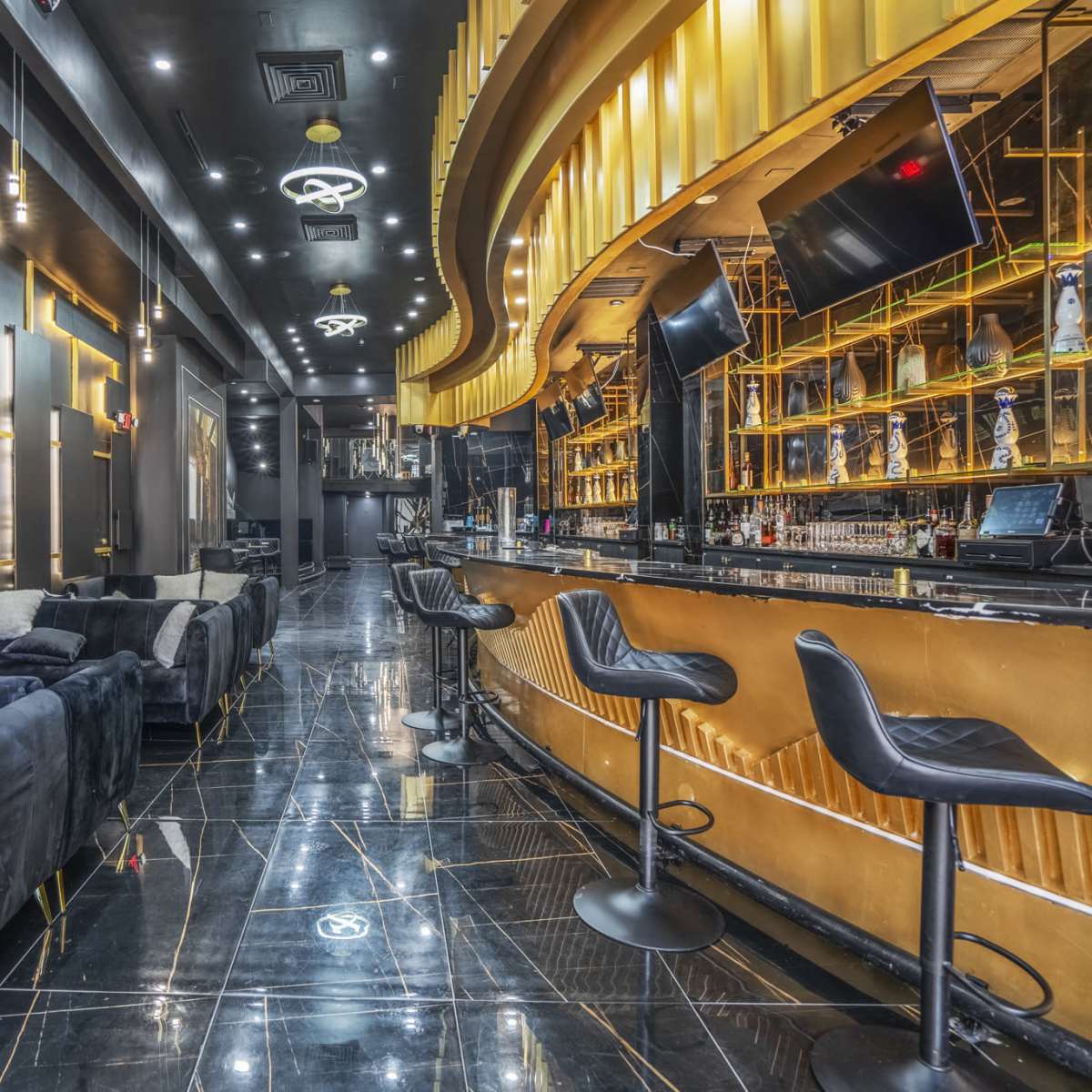 A sleek bar area features a glossy black marble floor, a curved gold bar, and plush seating against dark walls.