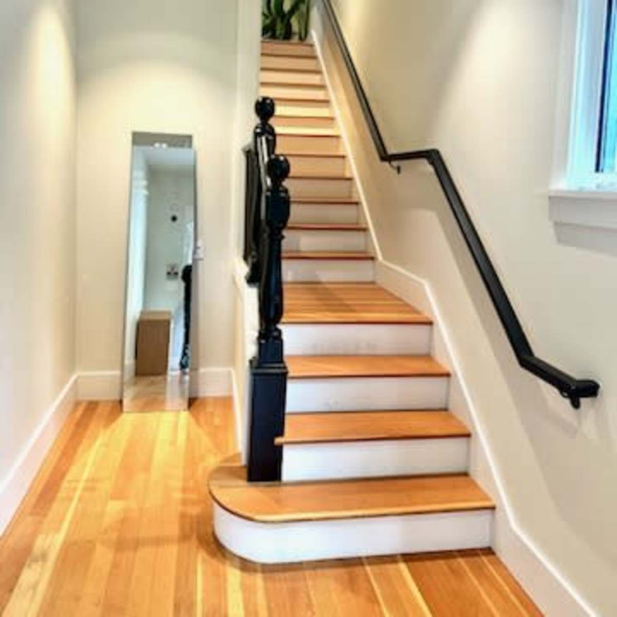 A staircase with wooden steps and a black handrail leads upward, flanked by light-colored walls and a small mirror.