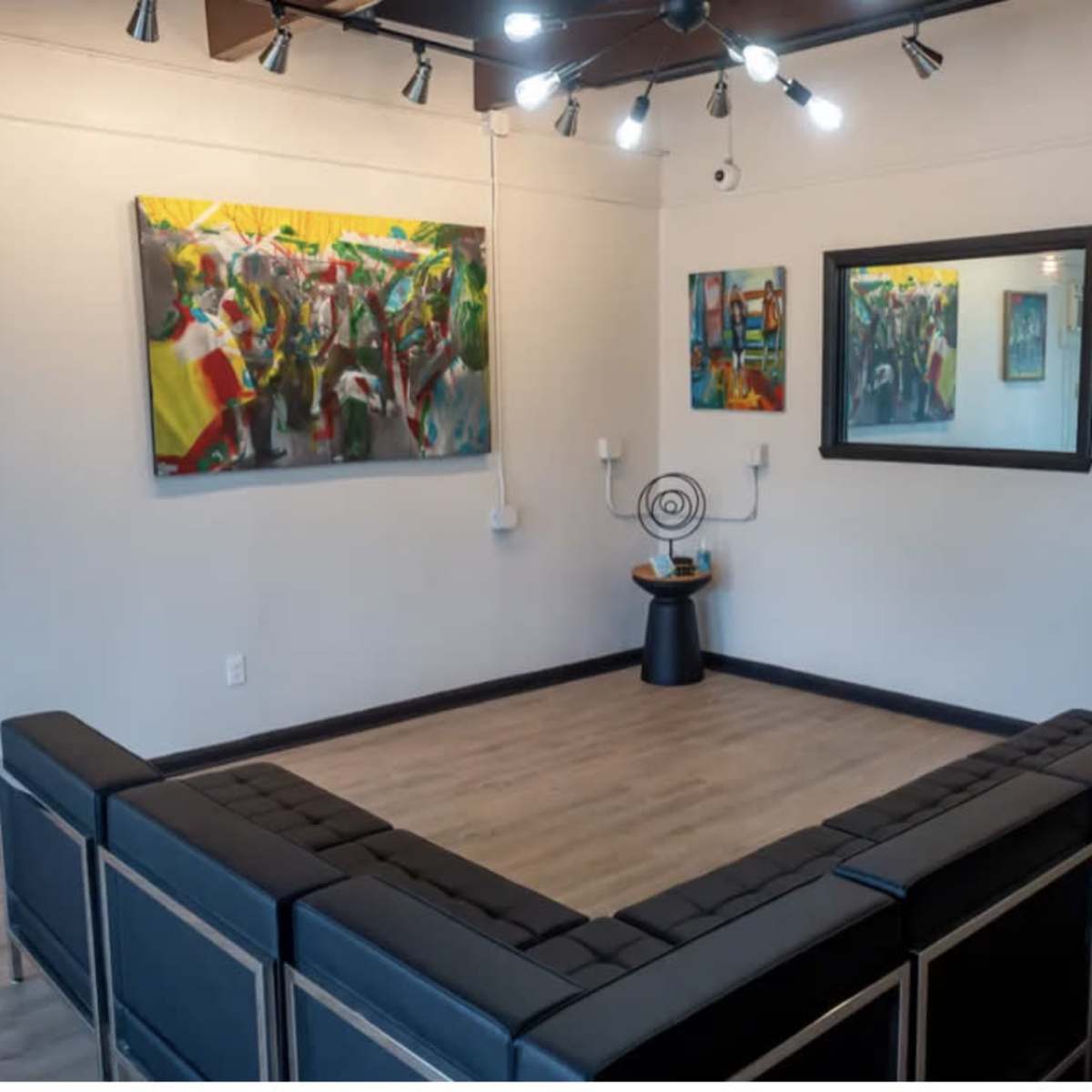 A modern art gallery with a U-shaped seating arrangement facing colorful paintings on the walls and a round decorative piece in the center.