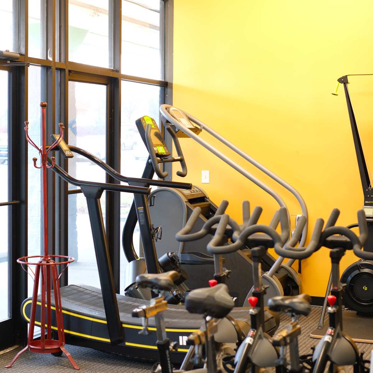 A fitness center interior with exercise equipment, including an elliptical and a treadmill, near a glass entrance.