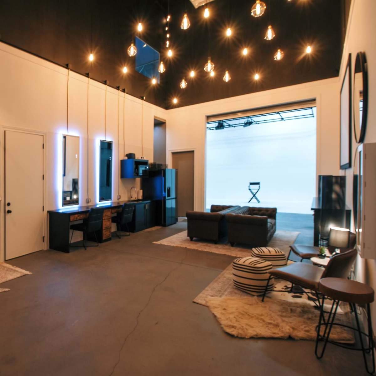 A modern studio space with several illuminated mirrors, a seating area with a couch, and a backdrop section for photography or filming.