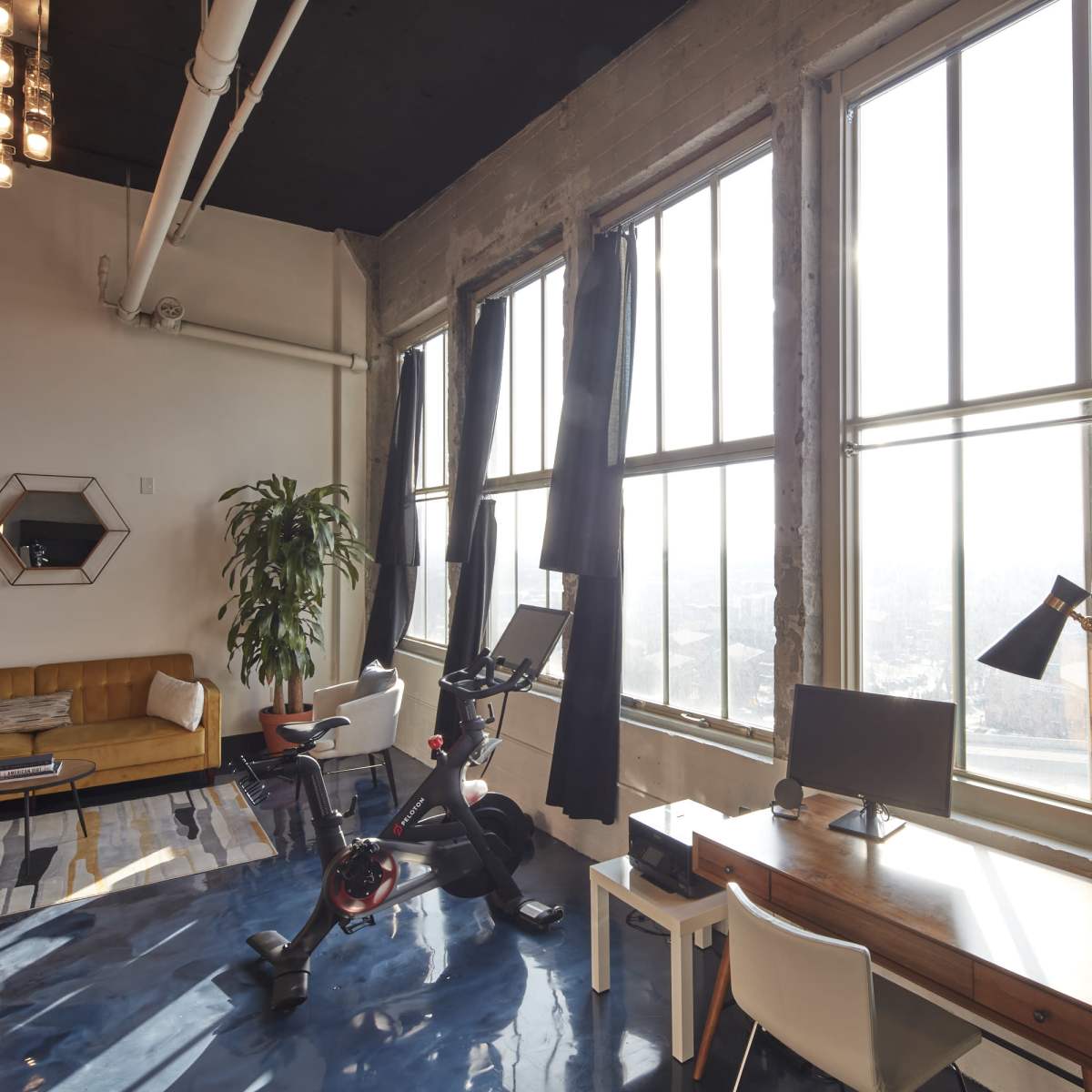 A modern room with large windows, a bicycle, a desk with a computer, a chair, and a sofa.