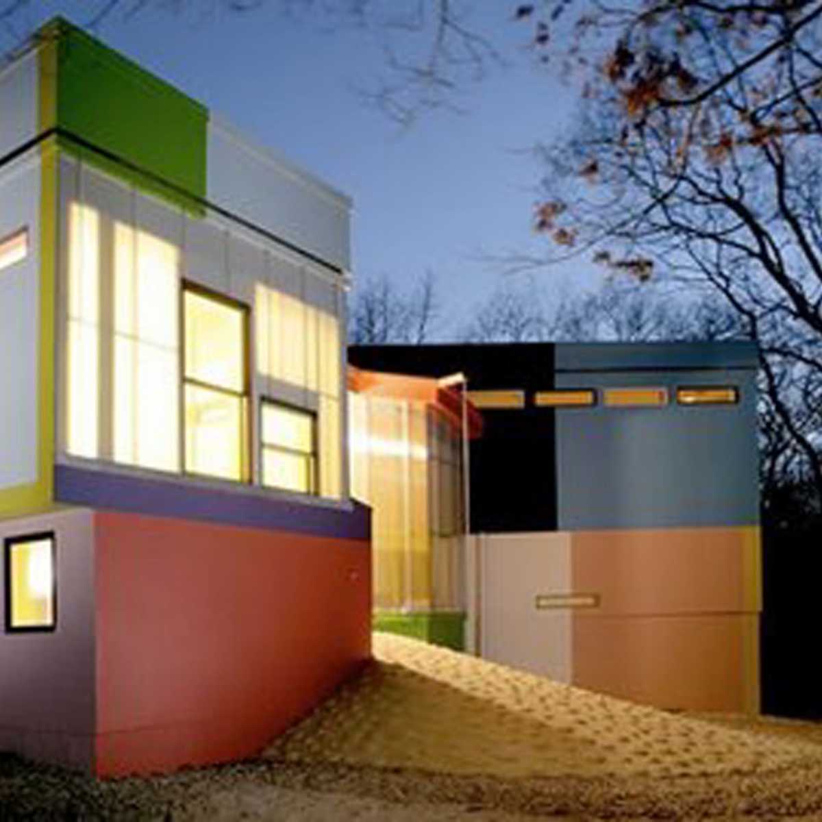 A modern, multicolored house is illuminated at dusk, showcasing a mix of angular shapes and large windows.
