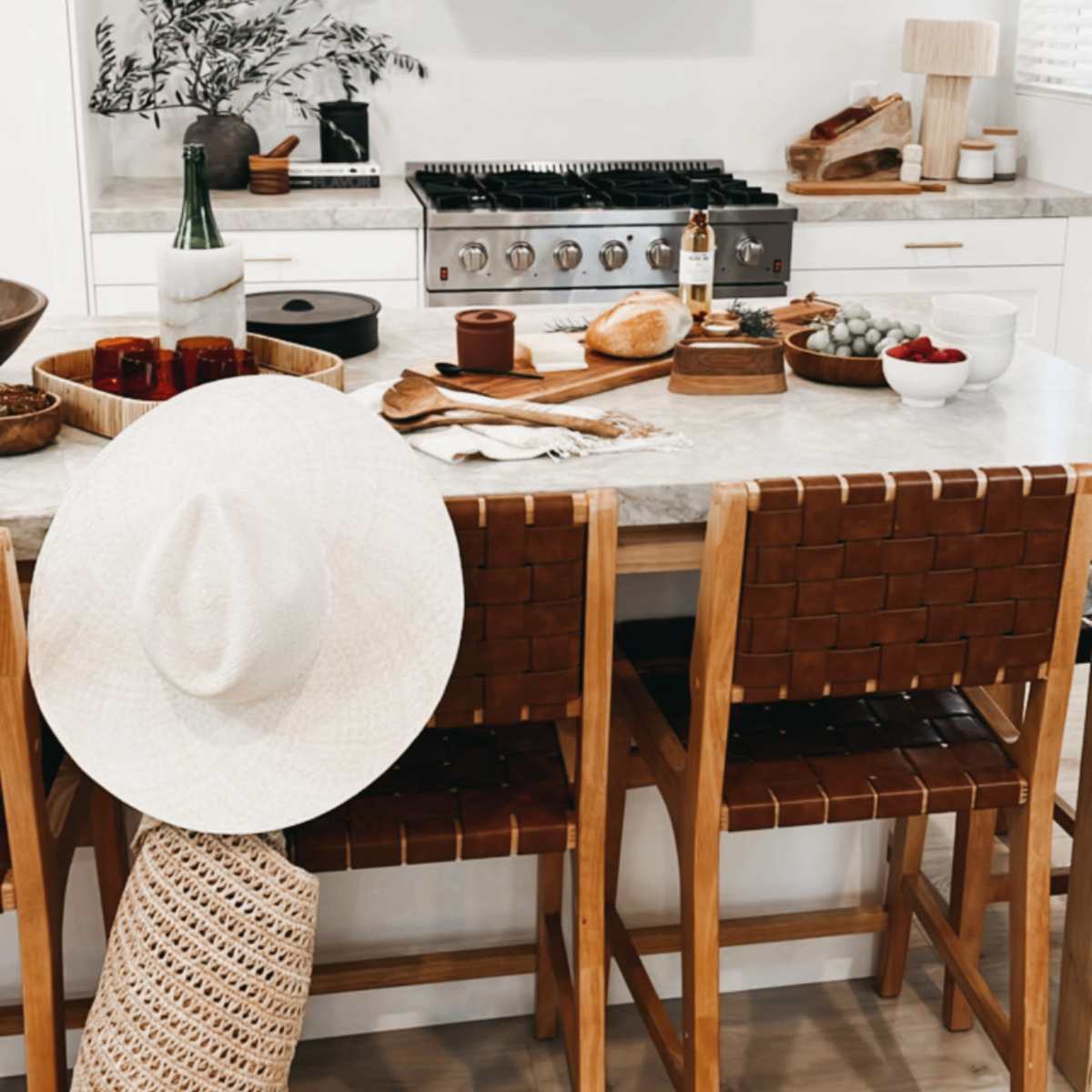 The kitchen features a modern design with a large gas stove, wooden bar stools, and a table set with various food items and decorative elements.