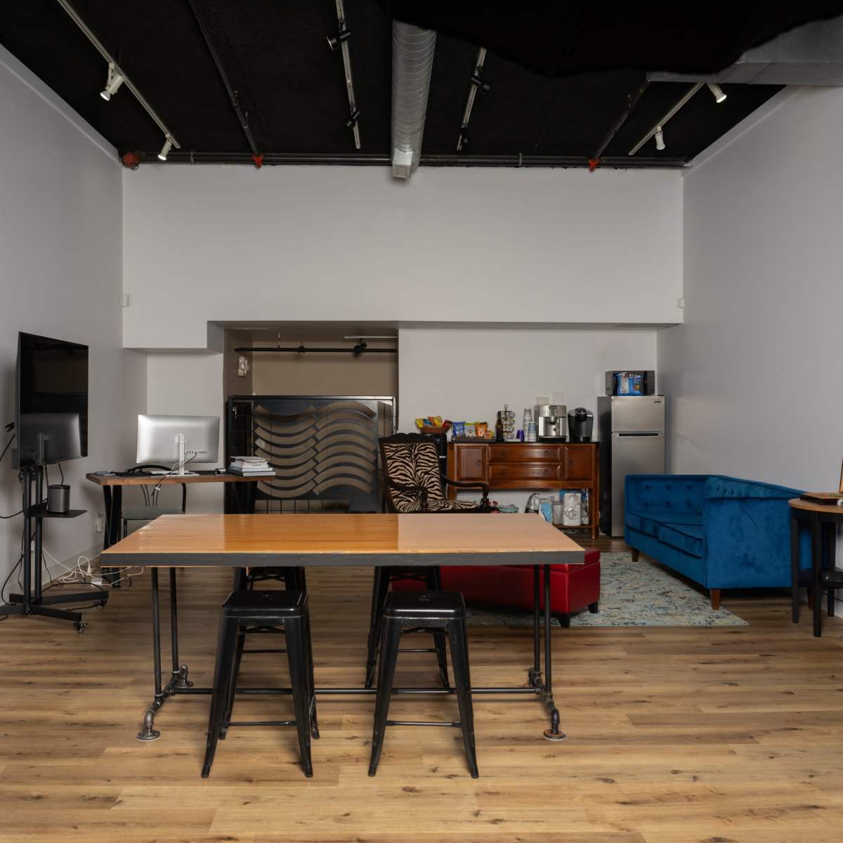 A modern kitchen and living area featuring a dining table with black stools, a blue couch, and various appliances along the walls.