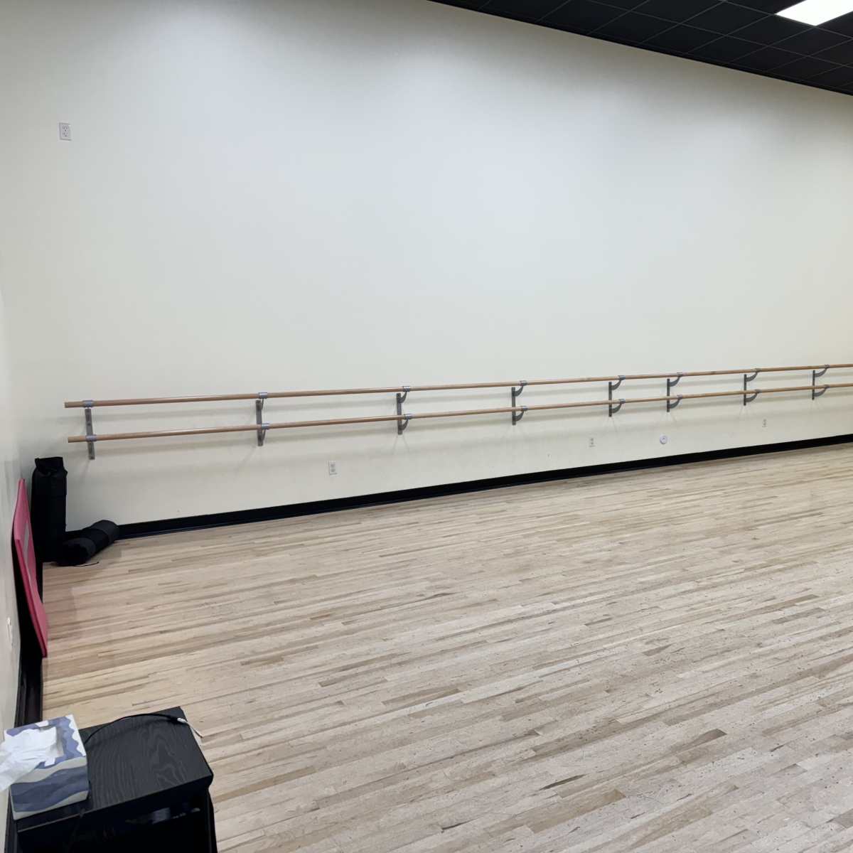 A spacious dance studio with polished wooden floors and ballet barres mounted on the wall.