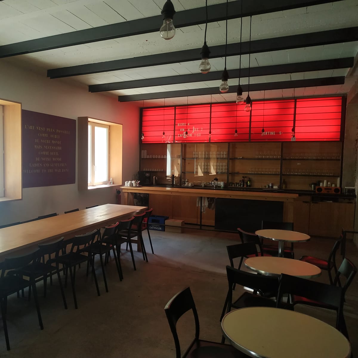 A spacious dining area with a long wooden table, chairs, and a kitchenette featuring a red backlit panel.
