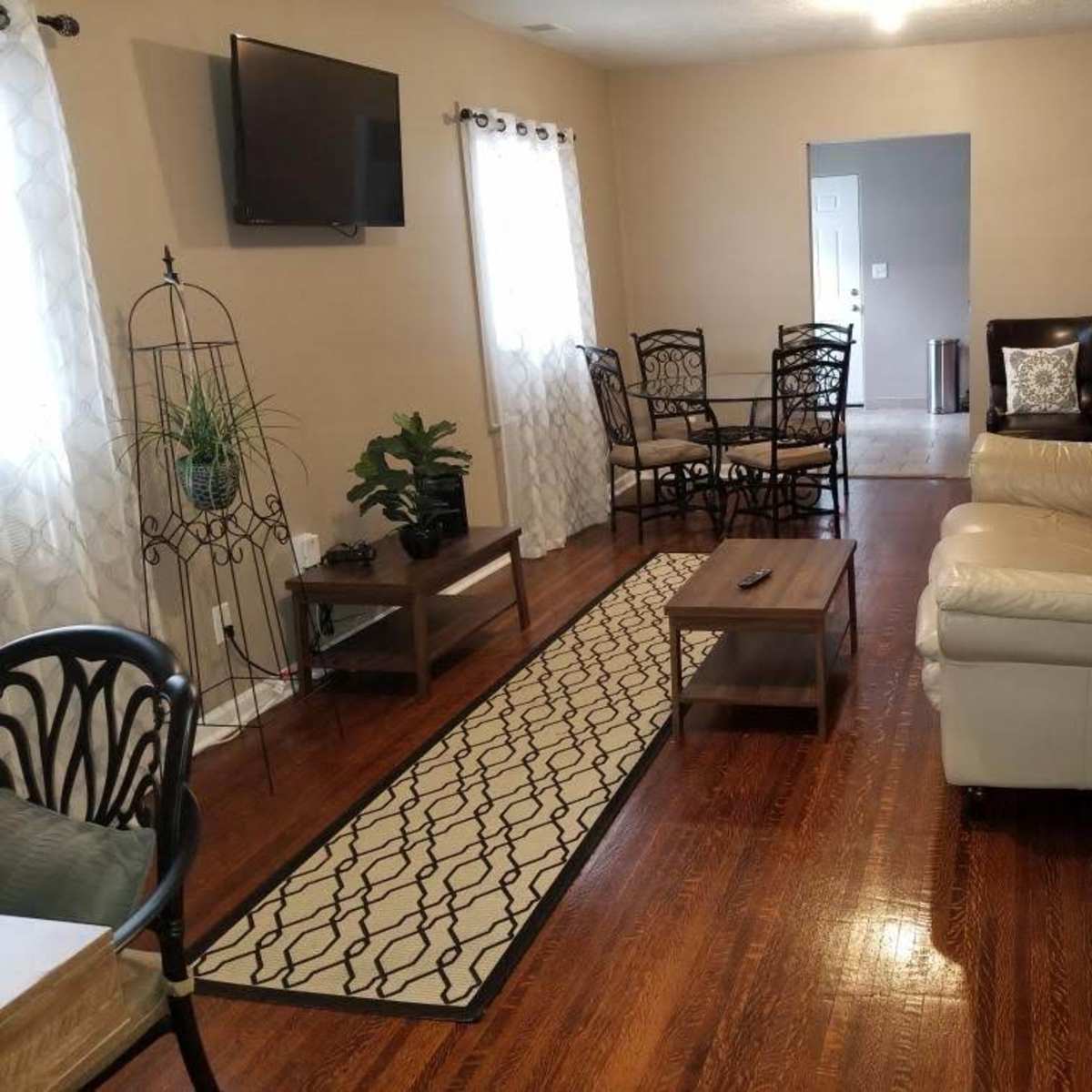 The living room features a white leather sofa, a coffee table, and a dining area with black chairs, all set on polished wood flooring.