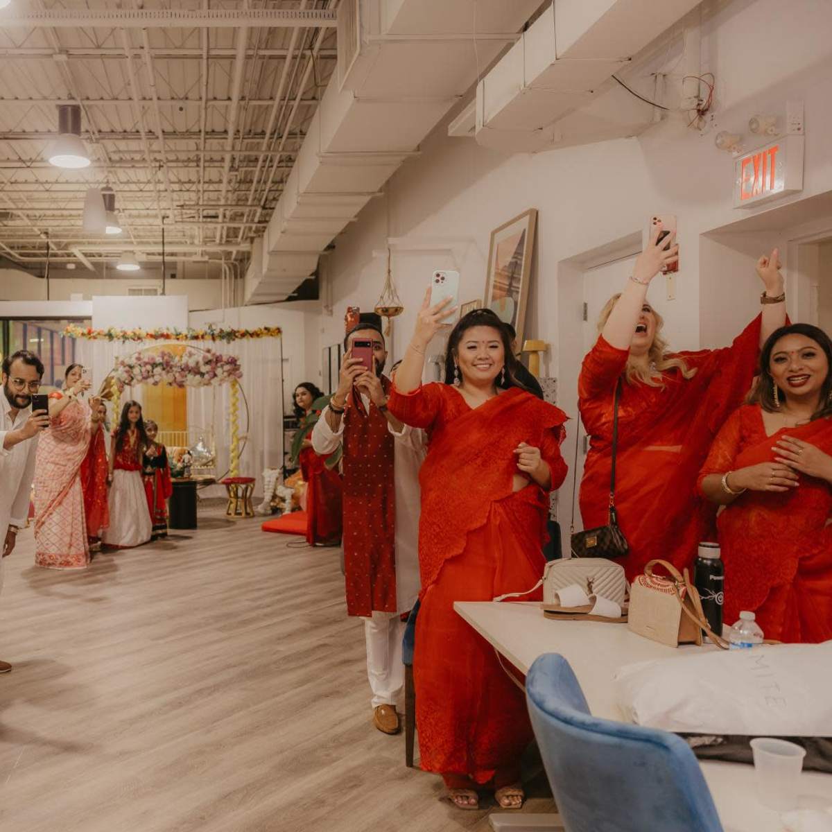 A group of people dressed in red clothing are gathered indoors, many of them holding smartphones to capture photos or videos at a celebration.