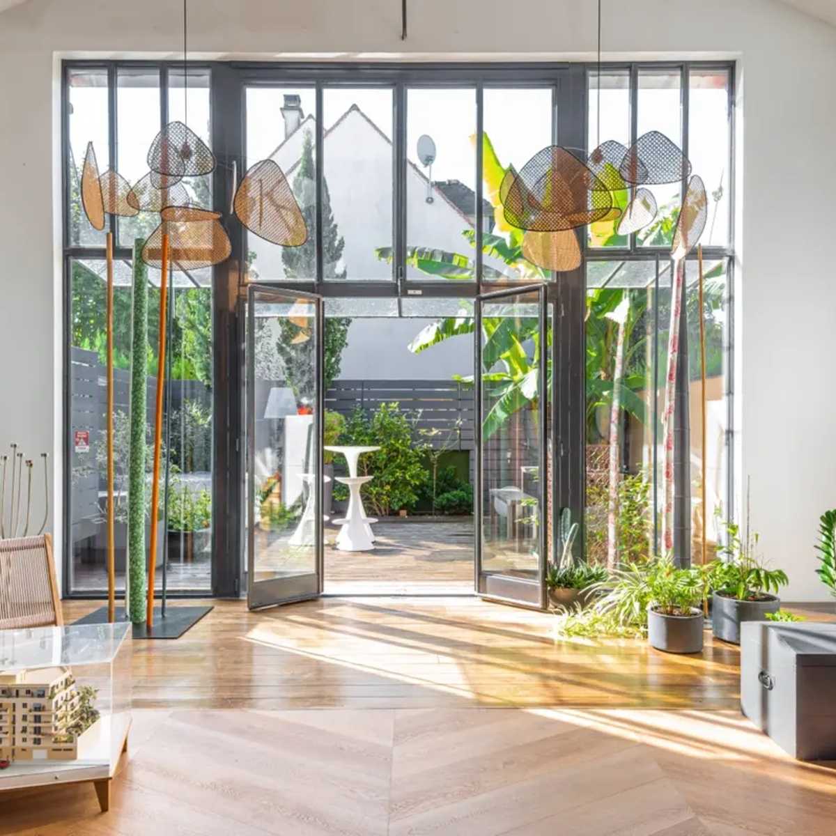 A modern interior space with large glass doors opening to a garden, featuring decorative screen sculptures and a model of a building on a table.
