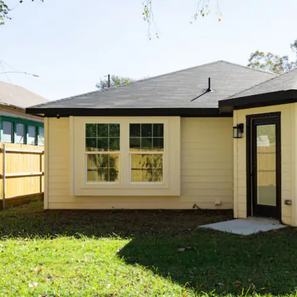 A single-story, light-colored house features a distinct octagonal bay window and several large windows on the front.