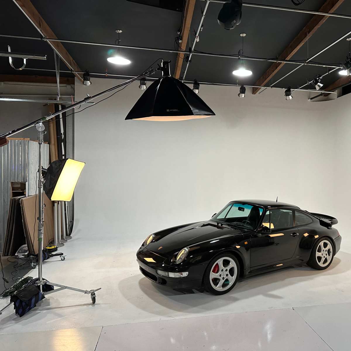 A black sports car is positioned in a studio with bright lighting and a white backdrop.