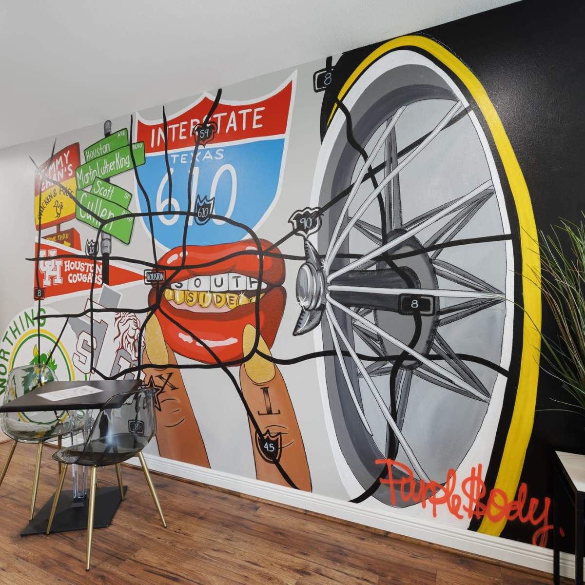 A vibrant mural on a wall featuring a bicycle wheel, a Texas highway sign, and playful graphics along with a small dining table and chairs set nearby.