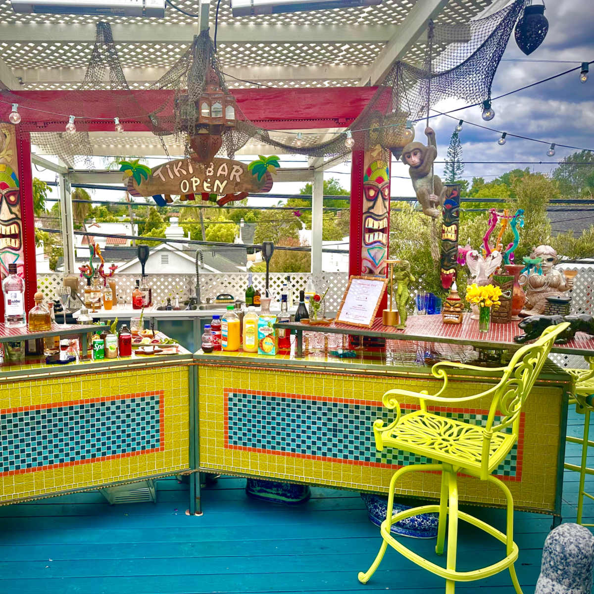 A brightly colored tiki bar with an array of liquor bottles, decorations, and seating under a covered outdoor area.