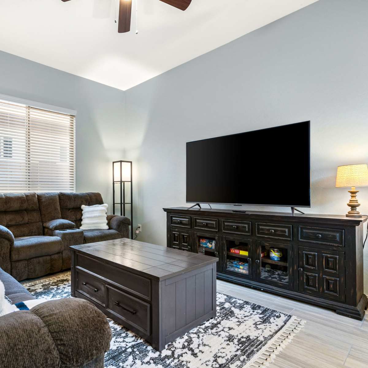 A living room features a dark wood coffee table, a large television on a matching console, and comfortable seating arranged around the space.