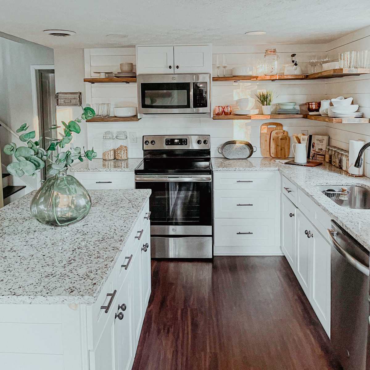 A modern kitchen with white cabinets, a stainless steel stove and microwave, and open shelves displaying various kitchenware.