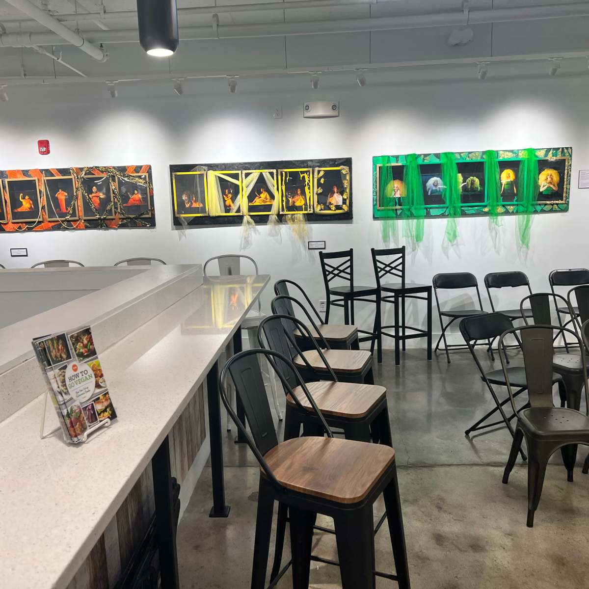 An art gallery with illuminated framed photographs hanging on the walls and empty chairs arranged in front of a countertop.