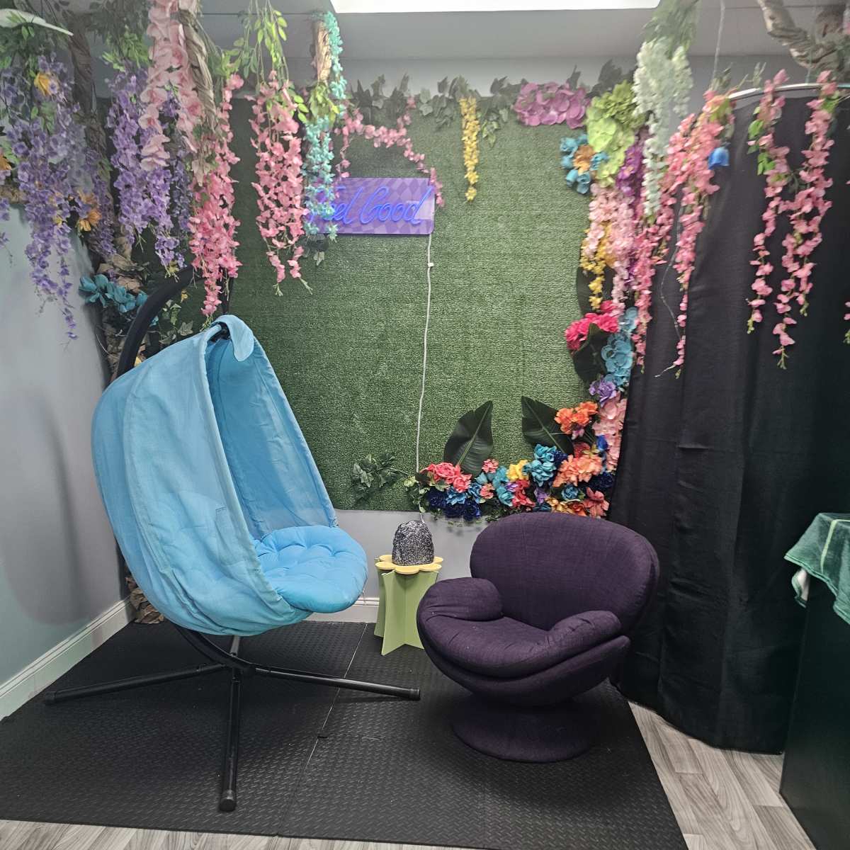 A cozy room decorated with vibrant artificial flowers, featuring a blue hanging chair and a purple circular chair on a wooden floor.